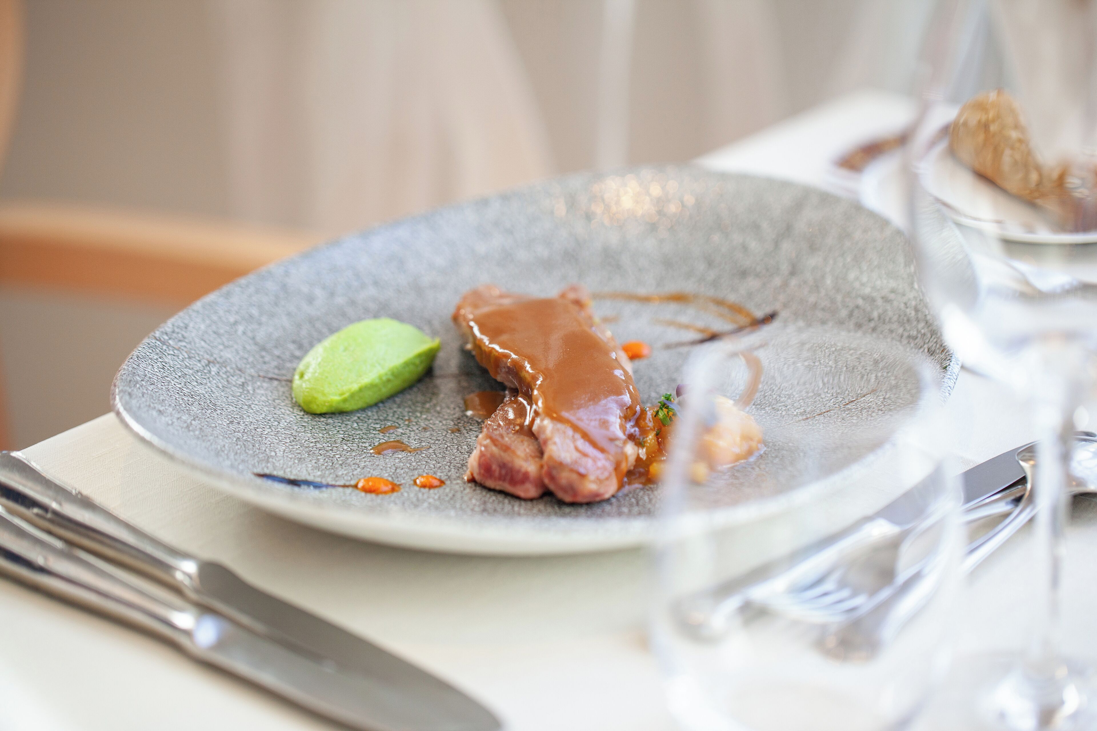 A plate with a piece of meat, a slice of avocado, and sauce.