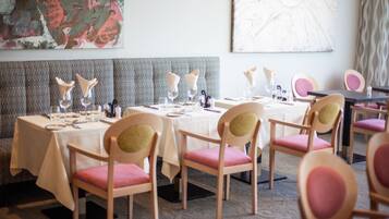 A dining area with tables set for four, each with pink upholstered chairs and white tablecloths.