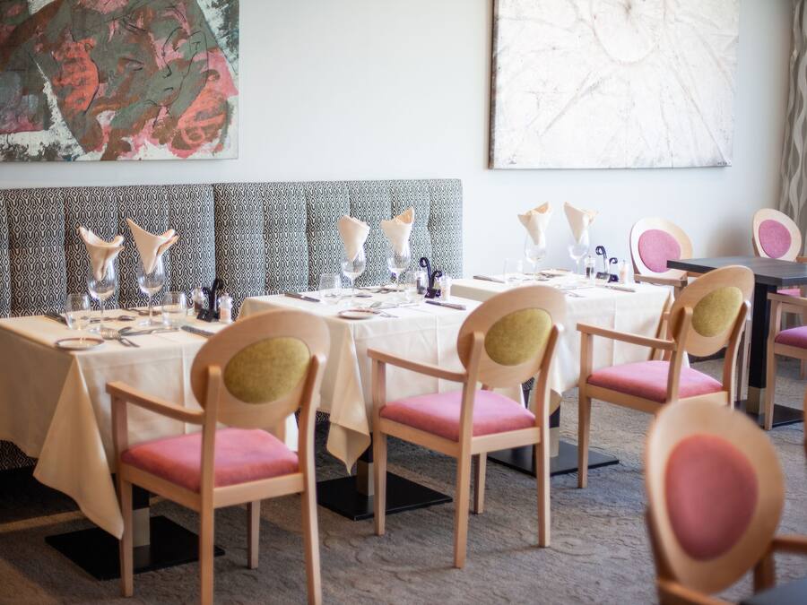 A dining area with tables set for four, each with pink upholstered chairs and white tablecloths.