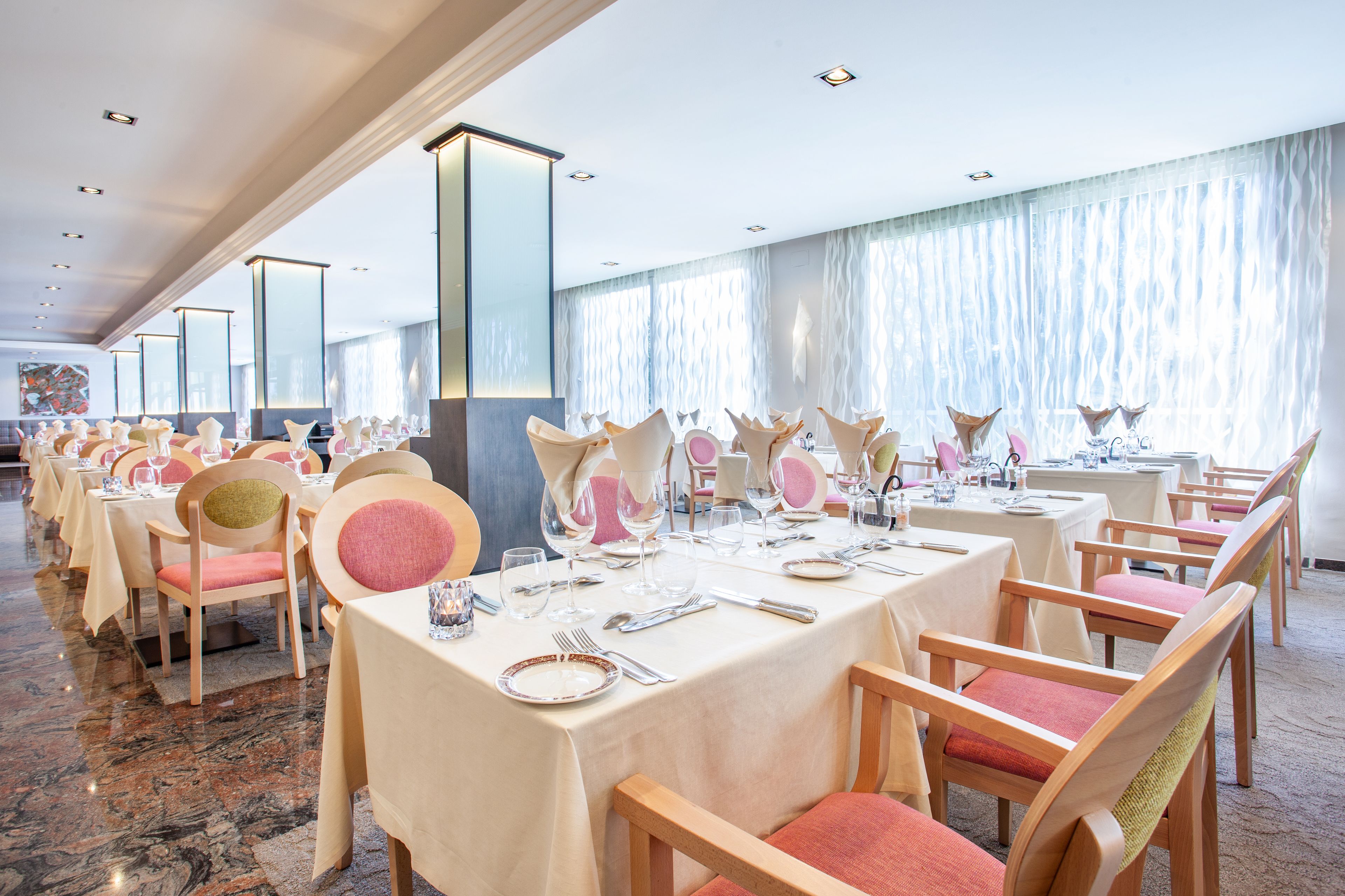 Un salón de banquetes con filas de mesas dispuestas para cenar, cada una con sillas y cubertería.