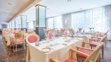 Un salón de banquetes con filas de mesas dispuestas para cenar, cada una con sillas y cubertería.