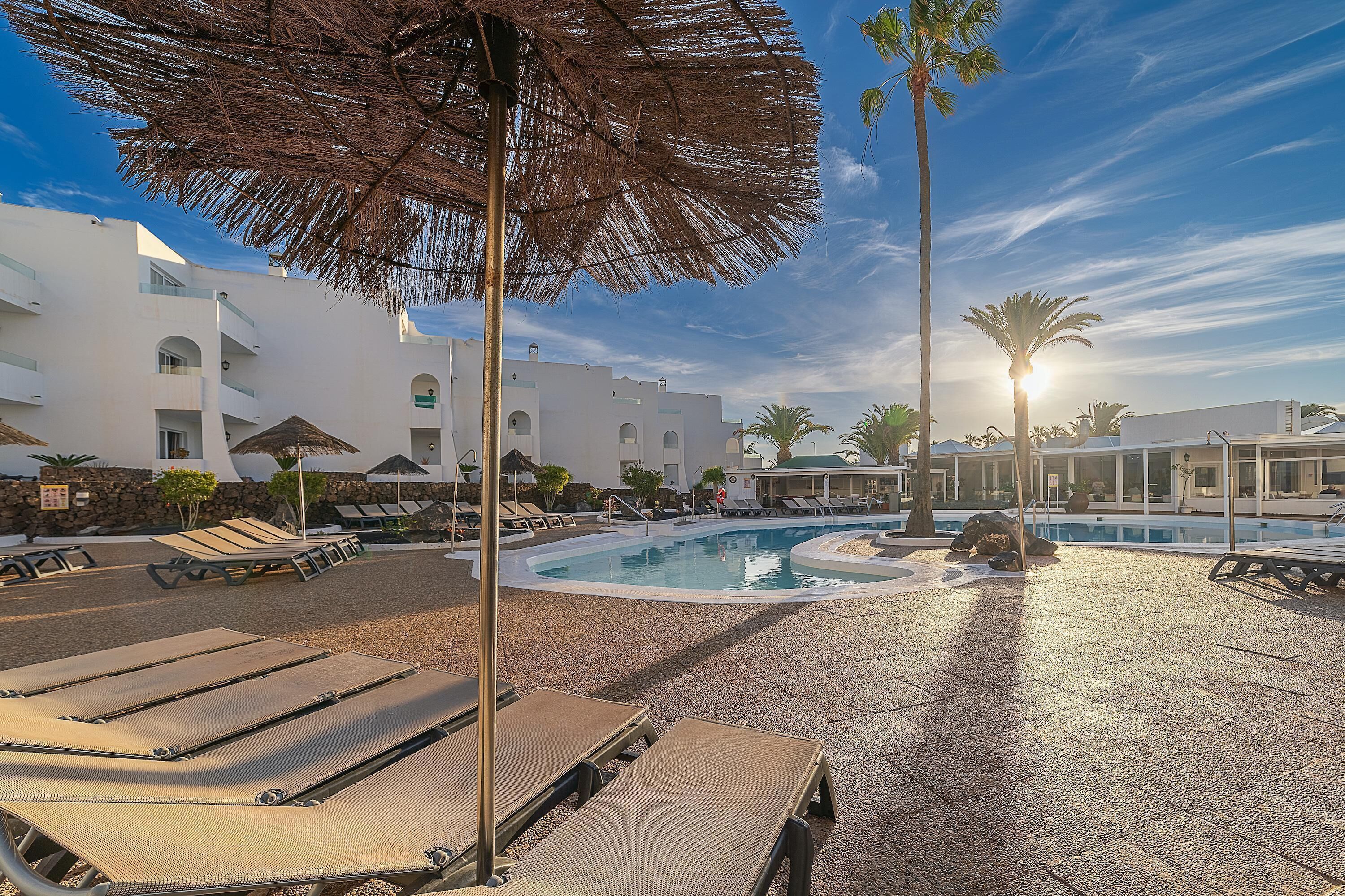 A pool area with sun loungers, umbrellas, and a clear sky.