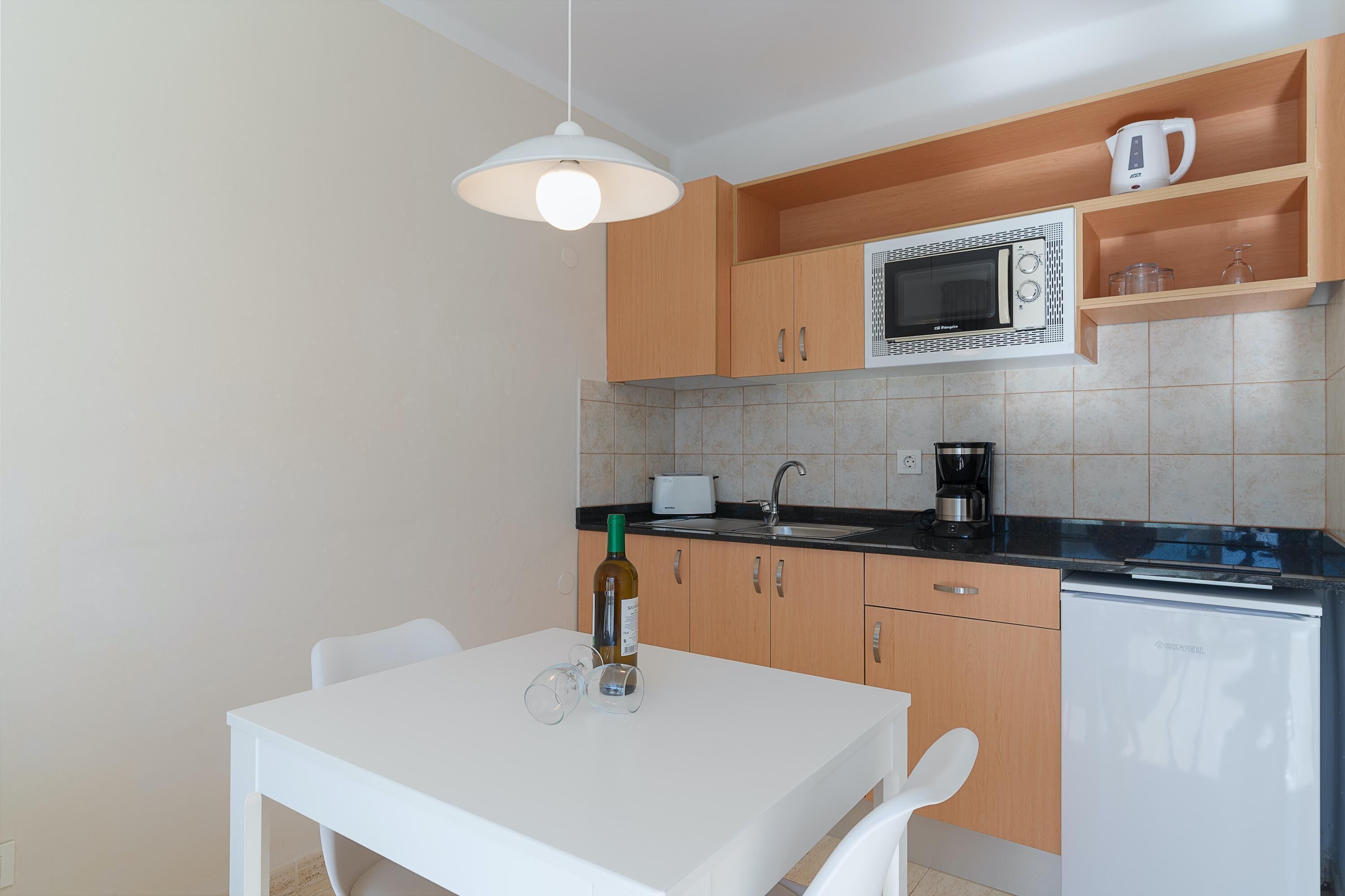 A modern kitchen with wooden cabinets, a white countertop, a microwave, a coffee maker, and a small refrigerator.