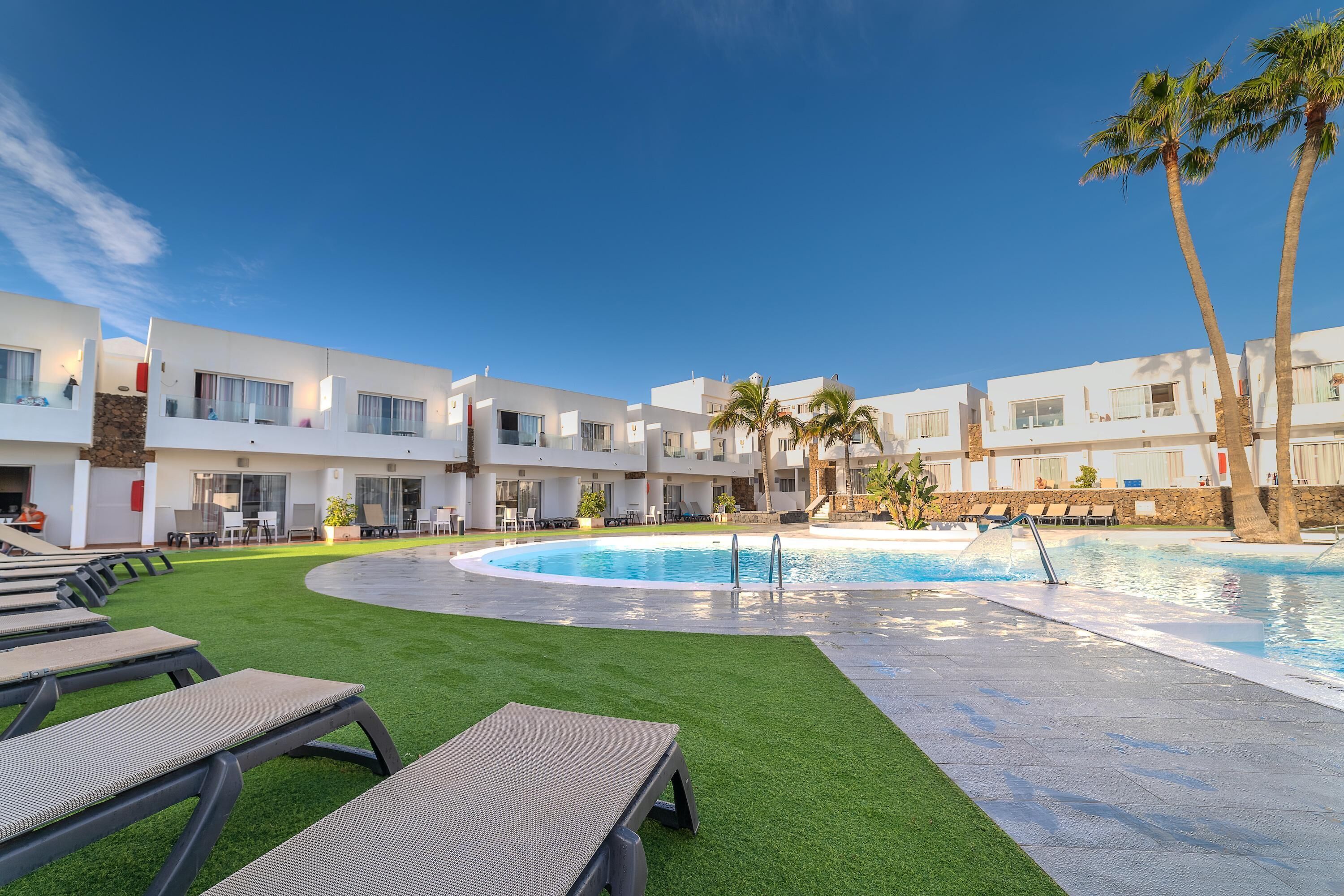 Un hotel moderno con piscina, césped verde y sillones de descanso.