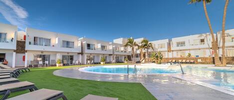 A modern hotel with a swimming pool, green lawn, and lounge chairs.