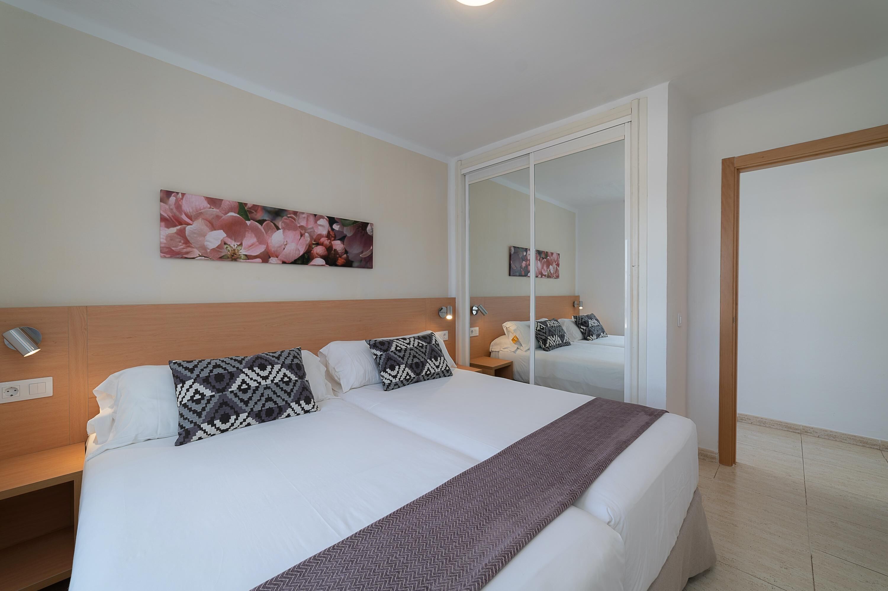 A hotel room with a large bed, a bedside table with a lamp, a wardrobe, and a wall-mounted artwork.