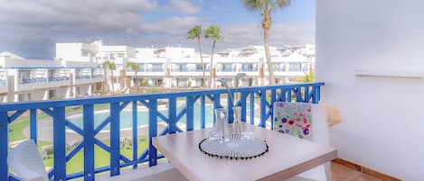 A balcony with a table, chairs, and a view of a pool and buildings.