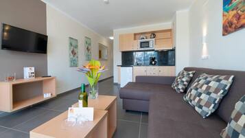 Una sala de estar moderna con un sofá, una mesa de centro y un televisor. Cuenta con una zona de cocina con armarios y un microondas.