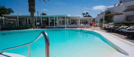 Ein Schwimmbecken mit Metallgeländer, Palmen und weißen Gebäuden mit Balkonen.
