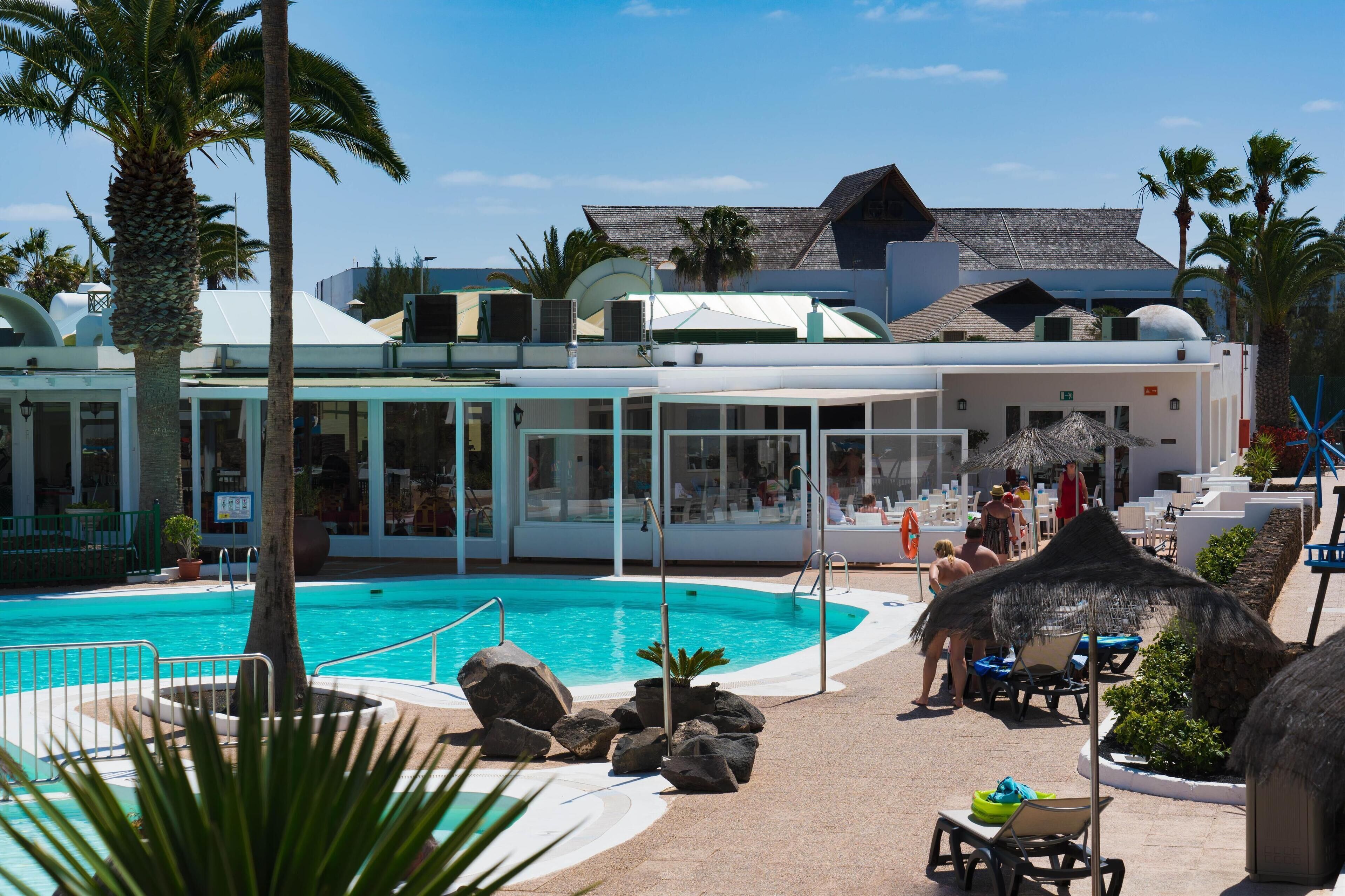 A pool area with lounge chairs, a palm tree, and a building with a modern design.