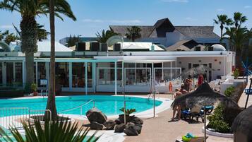 A pool area with lounge chairs, a palm tree, and a building with a modern design.