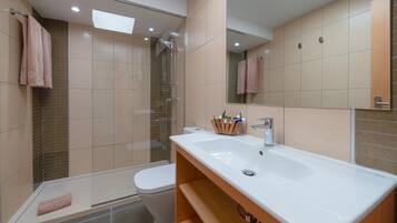 A modern bathroom with a glass shower enclosure, a white sink, and a toilet.