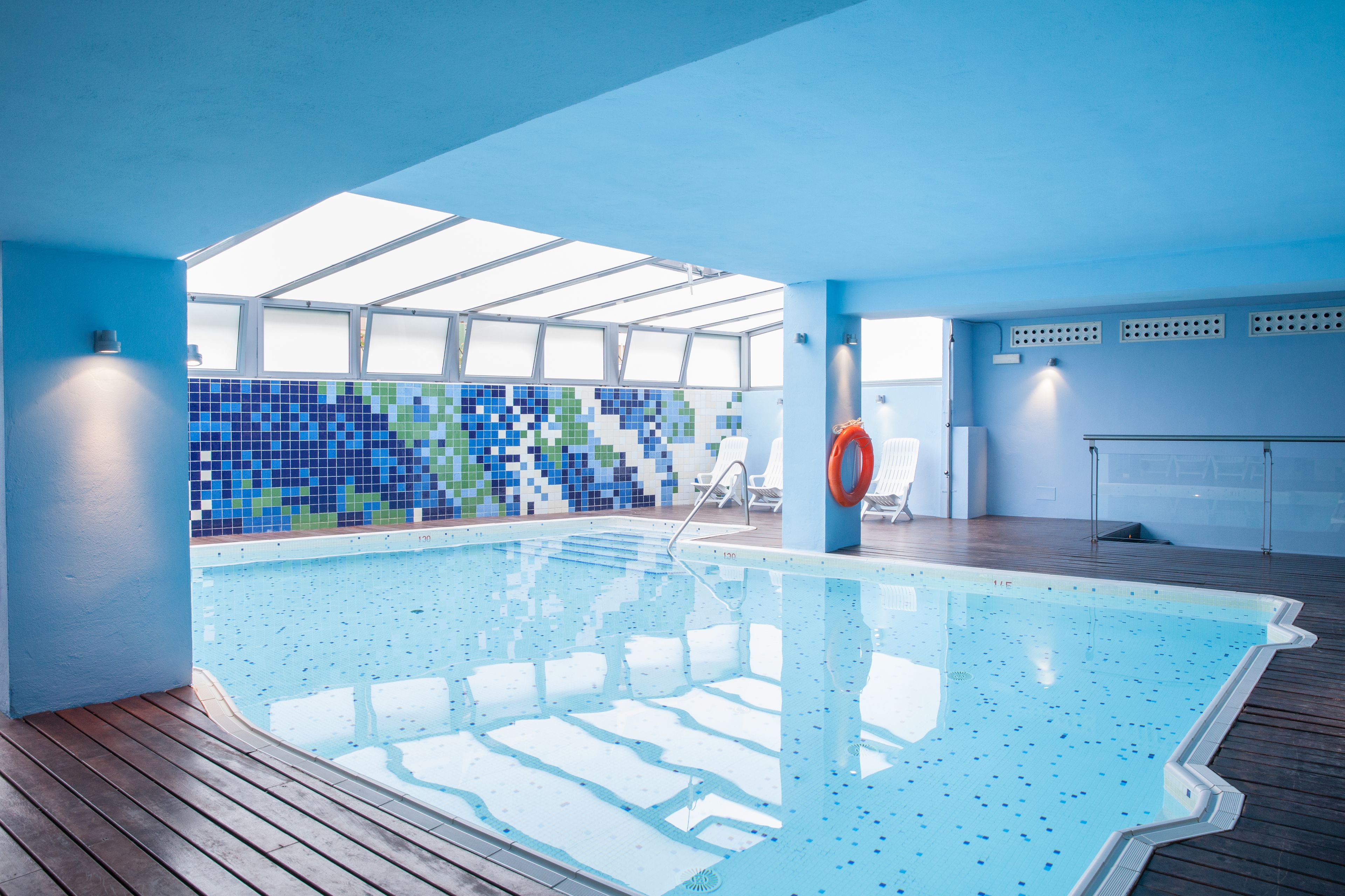 An indoor swimming pool with a tiled wall, wooden deck, and a ceiling with skylights.