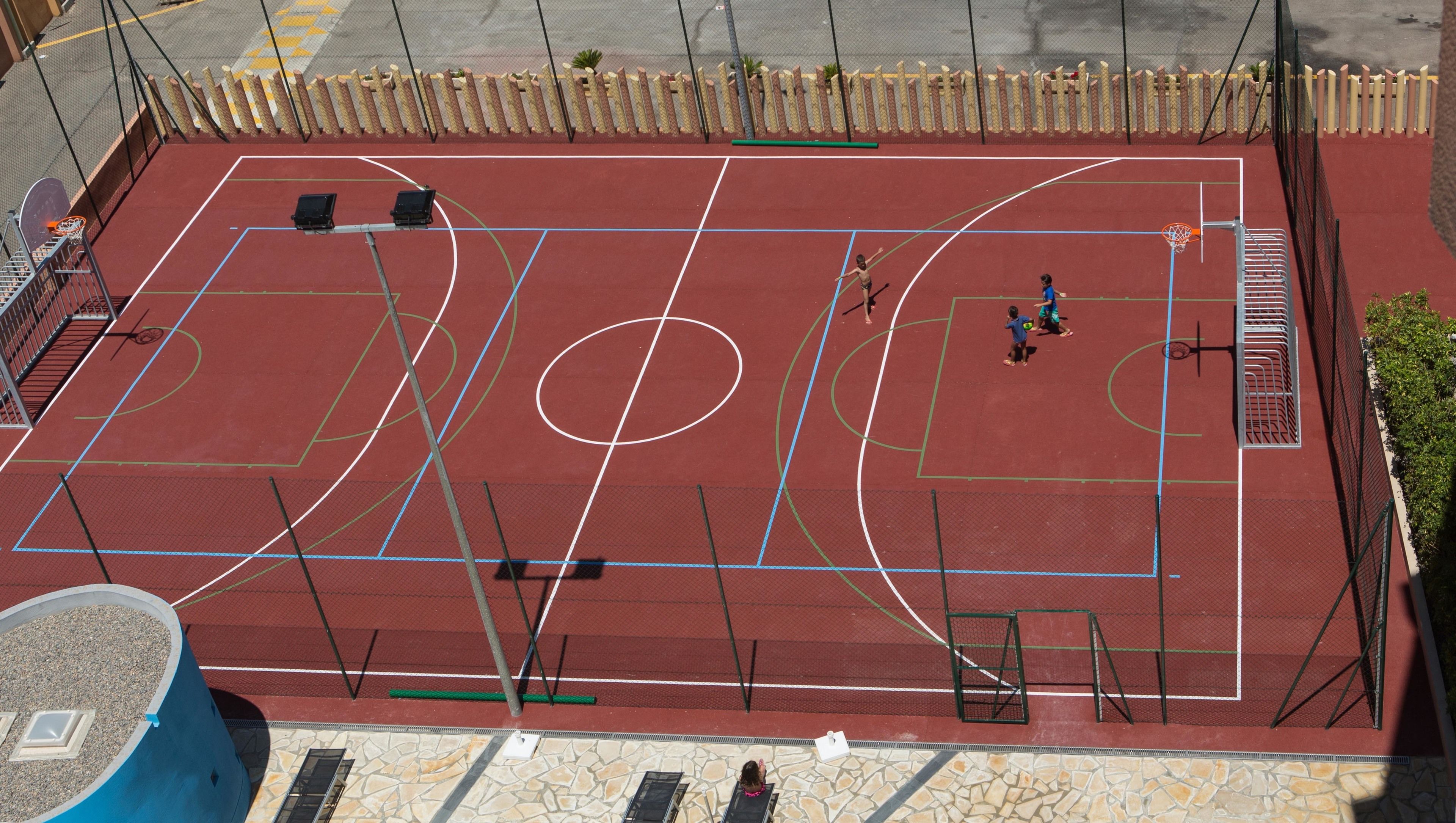 A basketball court with a net, two basketball hoops, and a fence around the perimeter.
