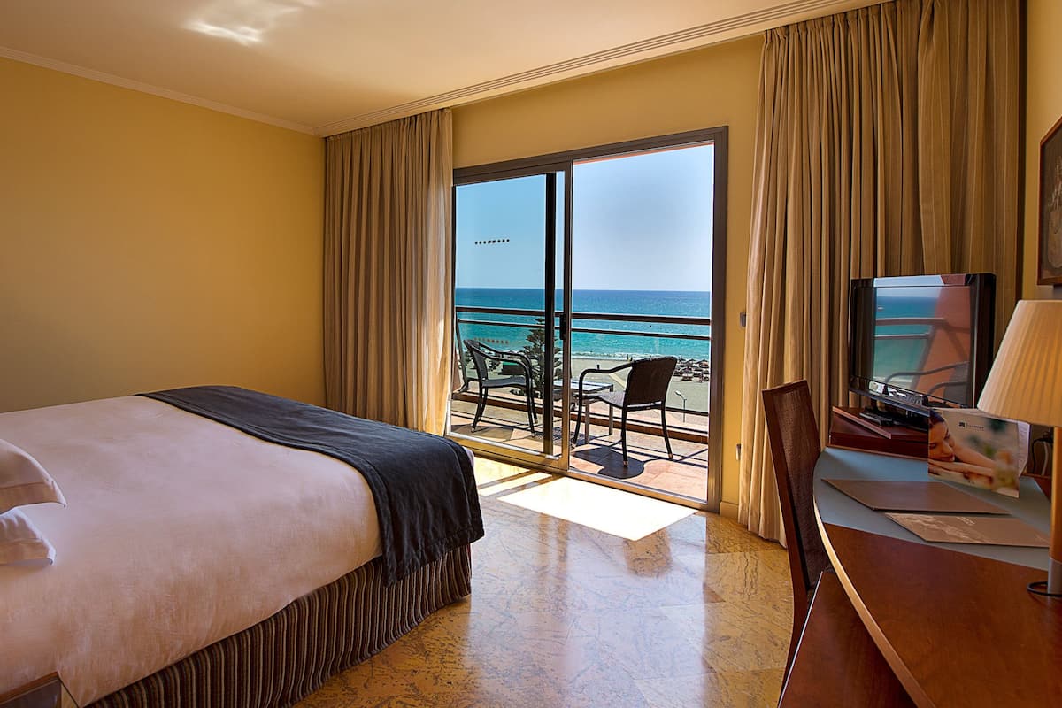 Une chambre d’hôtel avec un lit, un bureau, une télévision et un balcon donnant sur l’océan.
