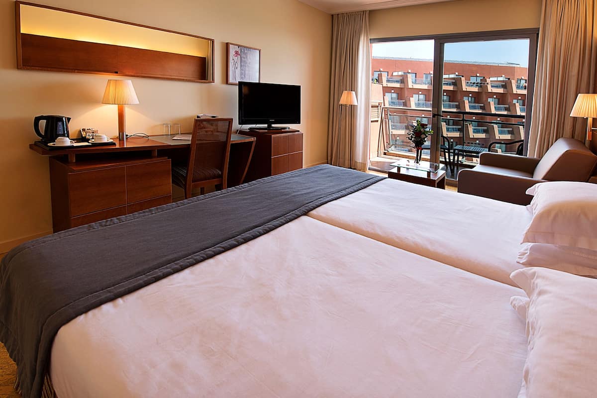 Une chambre d’hôtel avec un grand lit, un bureau avec une télévision, une chaise et une vue sur un immeuble par la fenêtre.