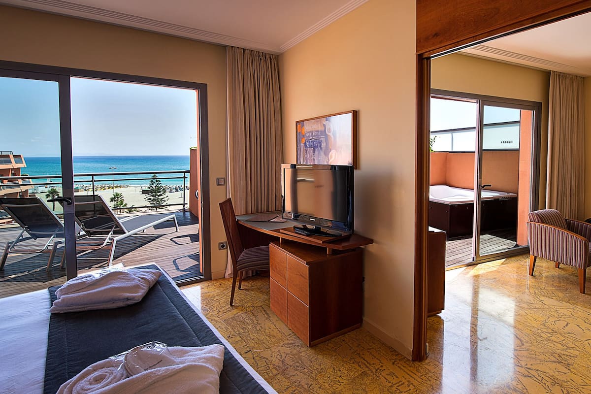 Une chambre d’hôtel avec balcon, un bureau, une télévision, un canapé et un coin repas.
