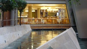 Ein moderner Essbereich im Innenbereich mit einem zentralen Wasserspiel, umgeben von Tischen und Stühlen.