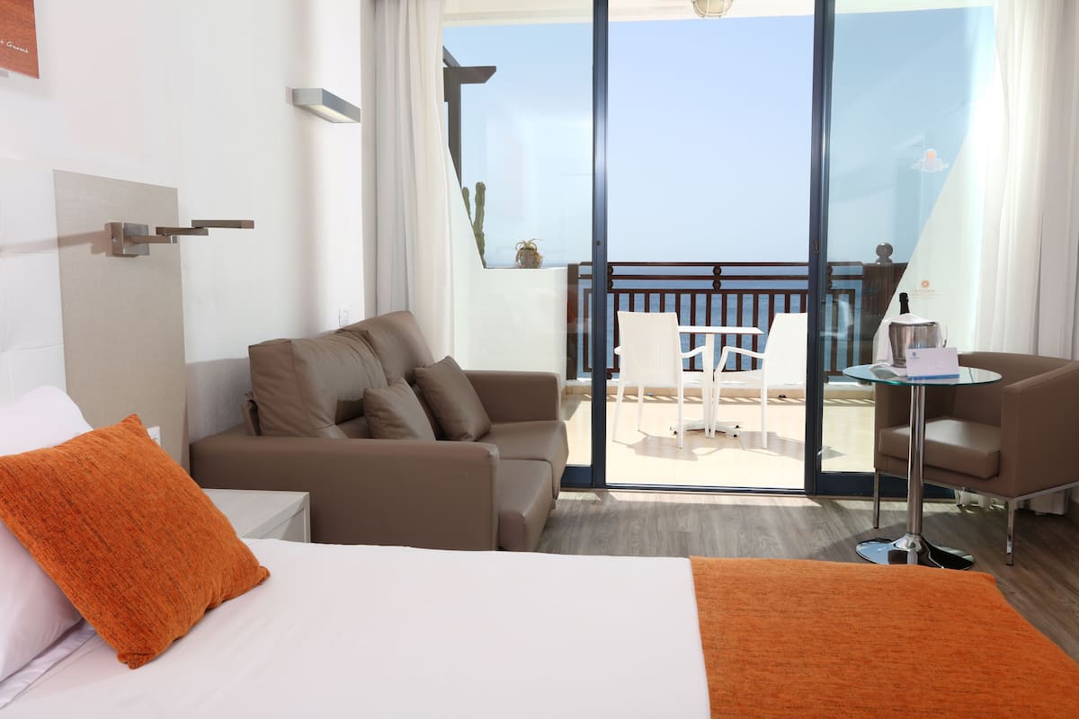 A hotel room with a bed, a sofa, a small table, and a balcony with a view.