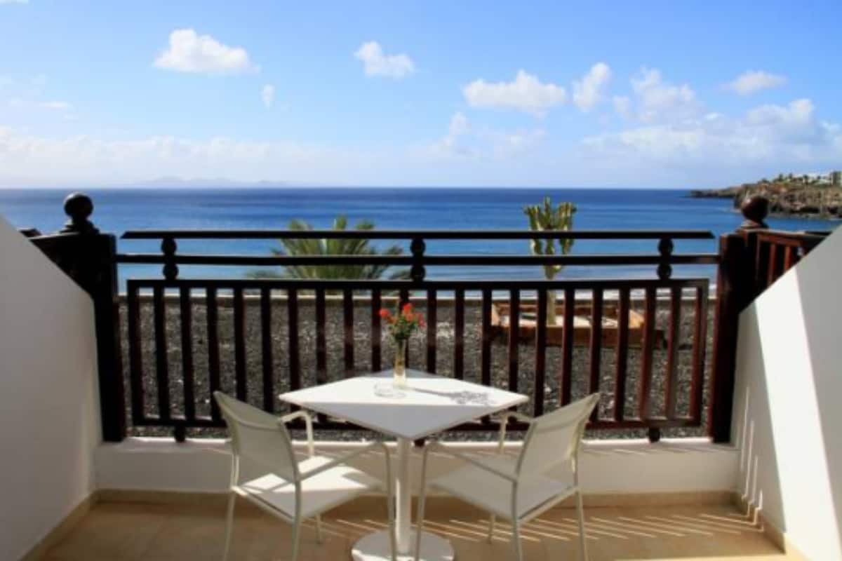 A balcony with a table and chairs, overlooking a beach and ocean.