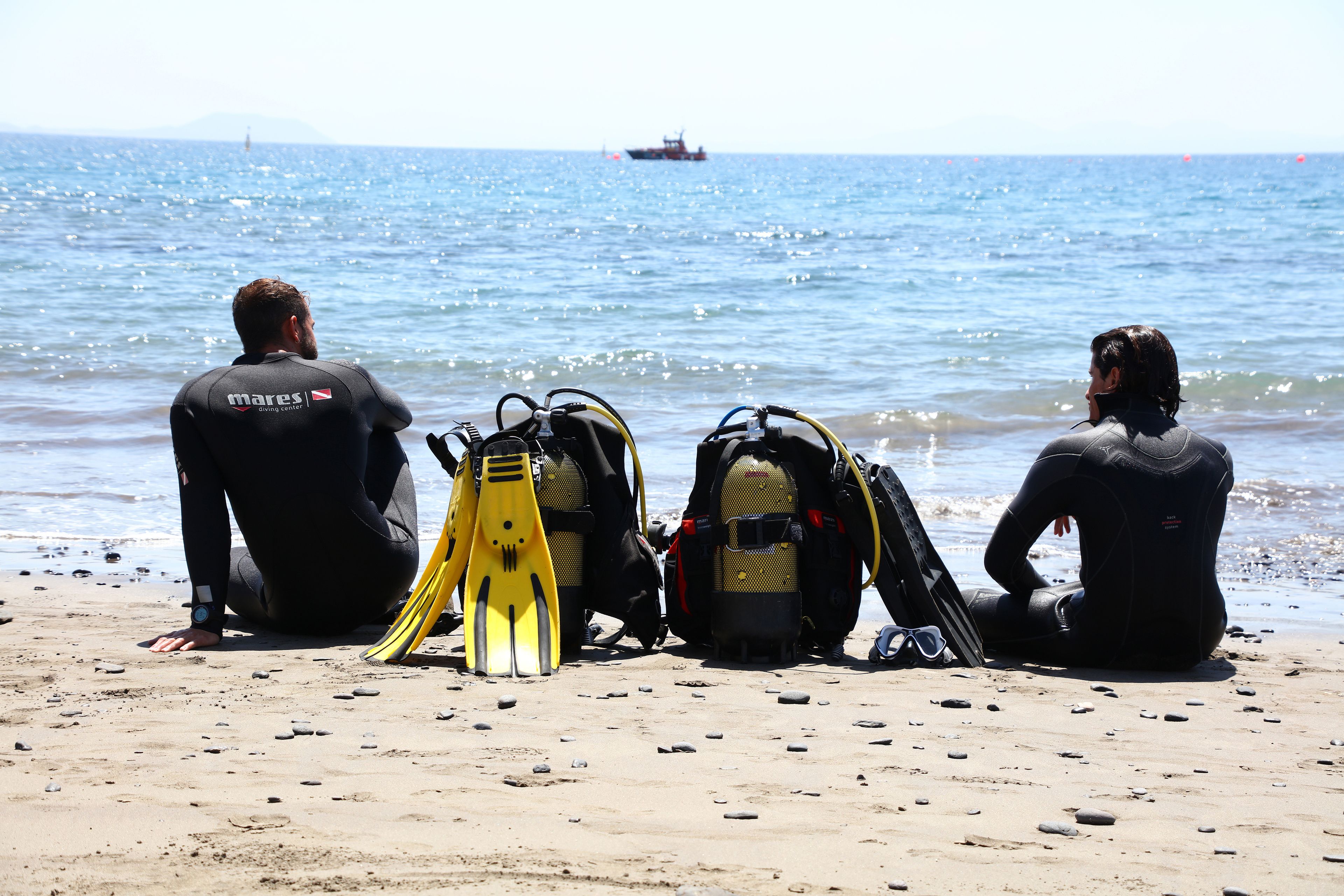 Three divers sitting on a beach with their diving gear and fins.