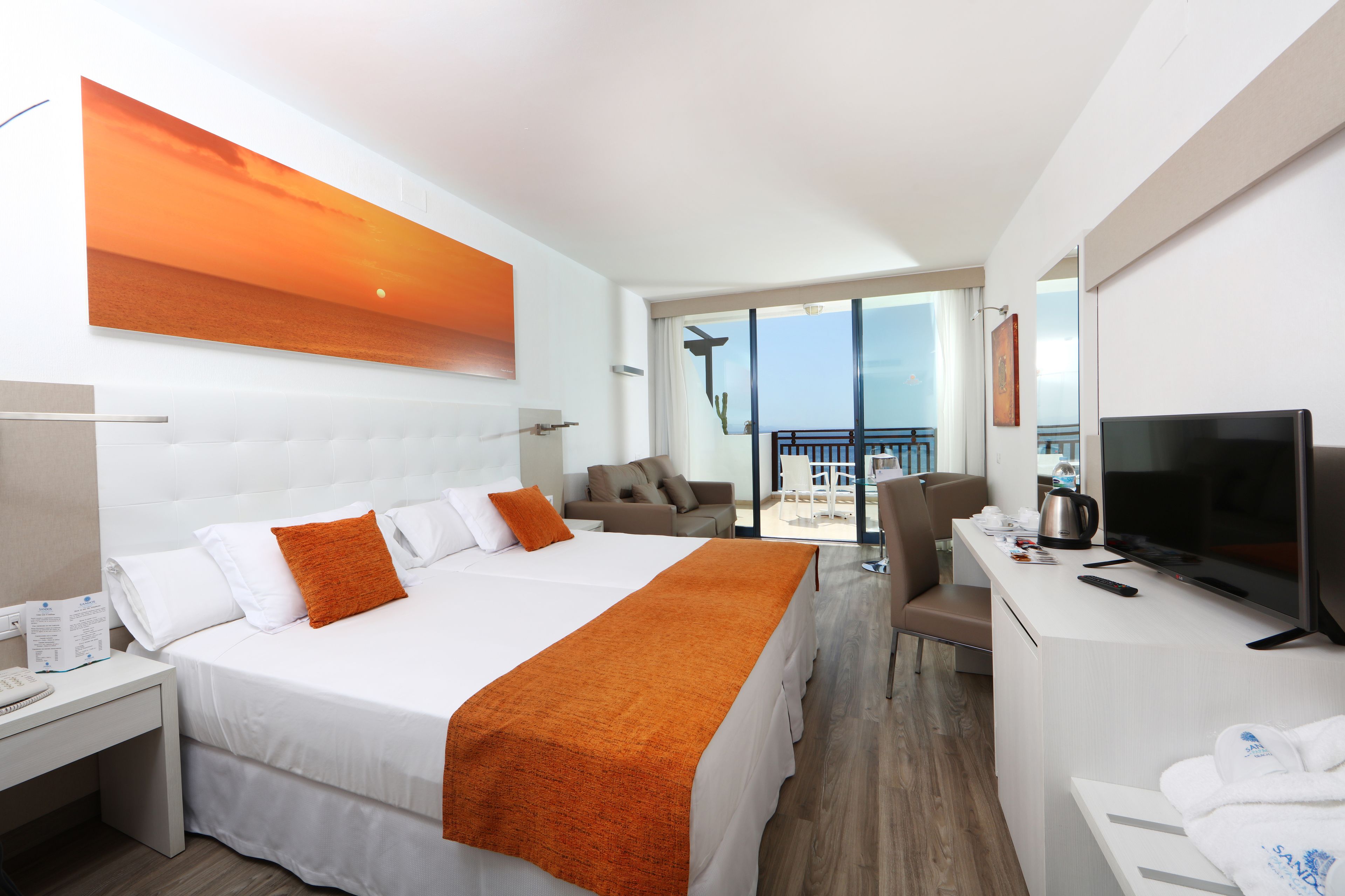 A hotel room with a large bed, a desk, a TV, and a balcony with a view.