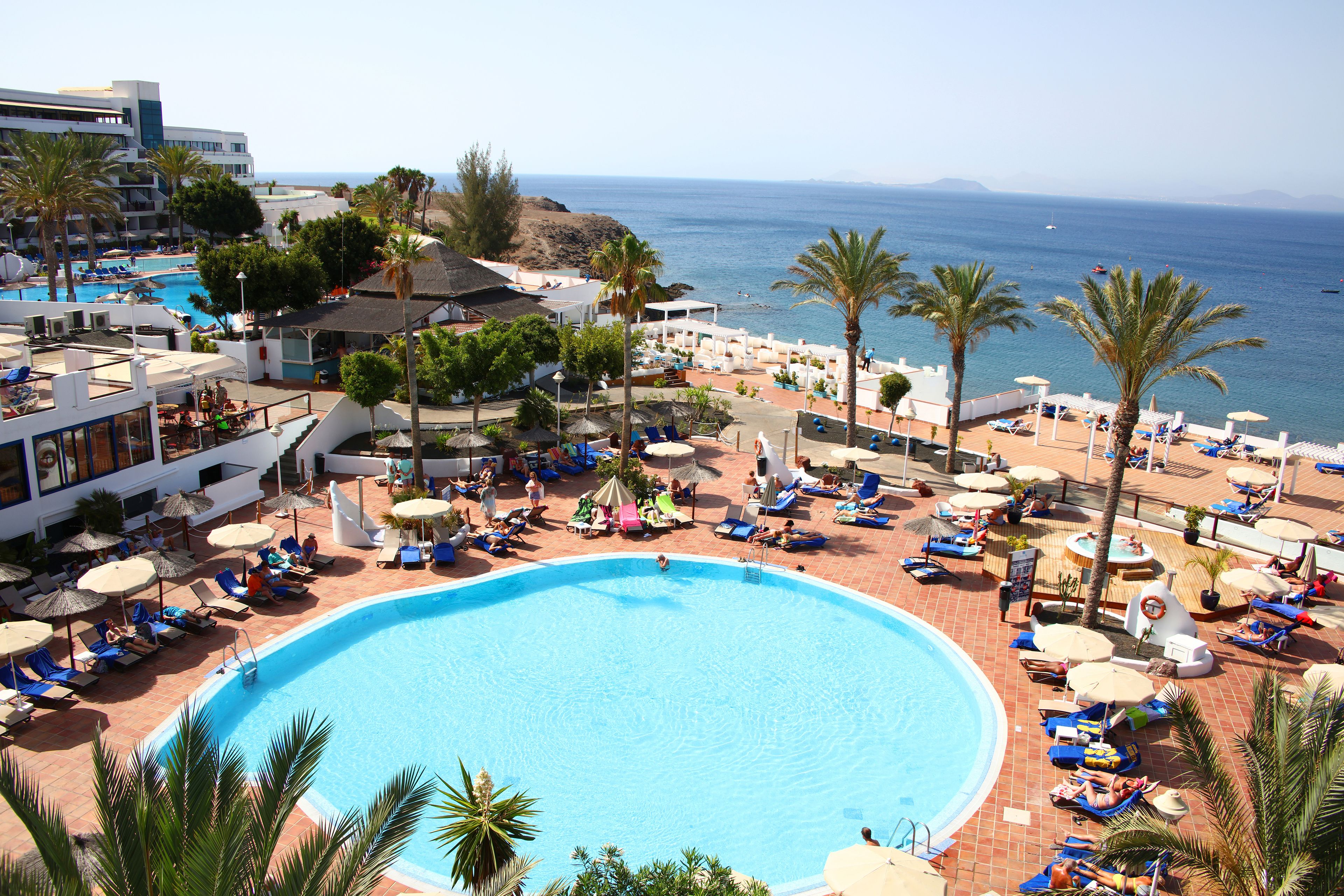 Et resort med en stor swimmingpool, liggestole, parasoller og havudsigt.