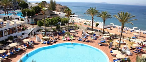 Et resort med en stor swimmingpool, liggestole, parasoller og havudsigt.