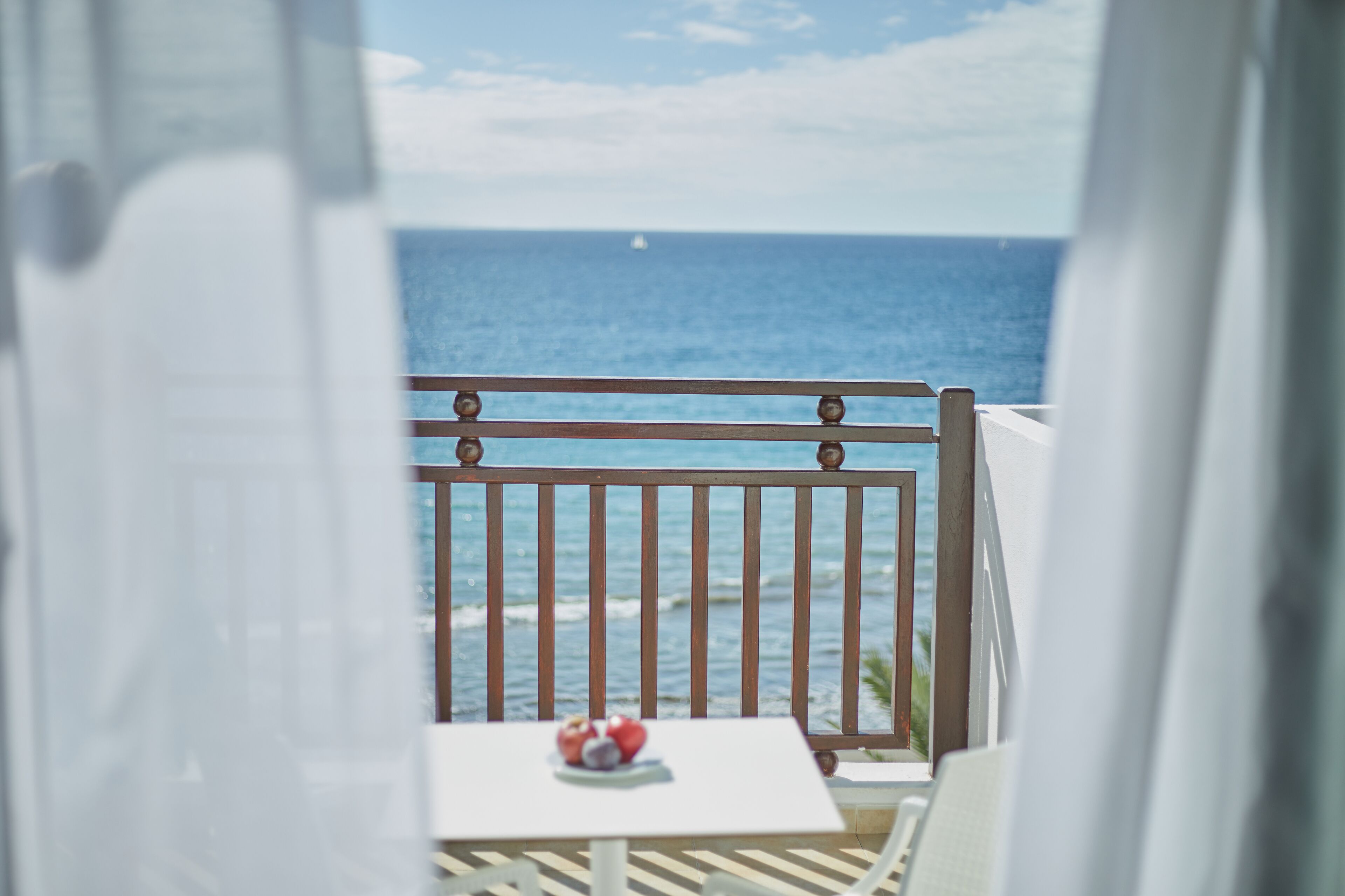 A balcony with a view of the ocean, a table with fruit, and a railing.