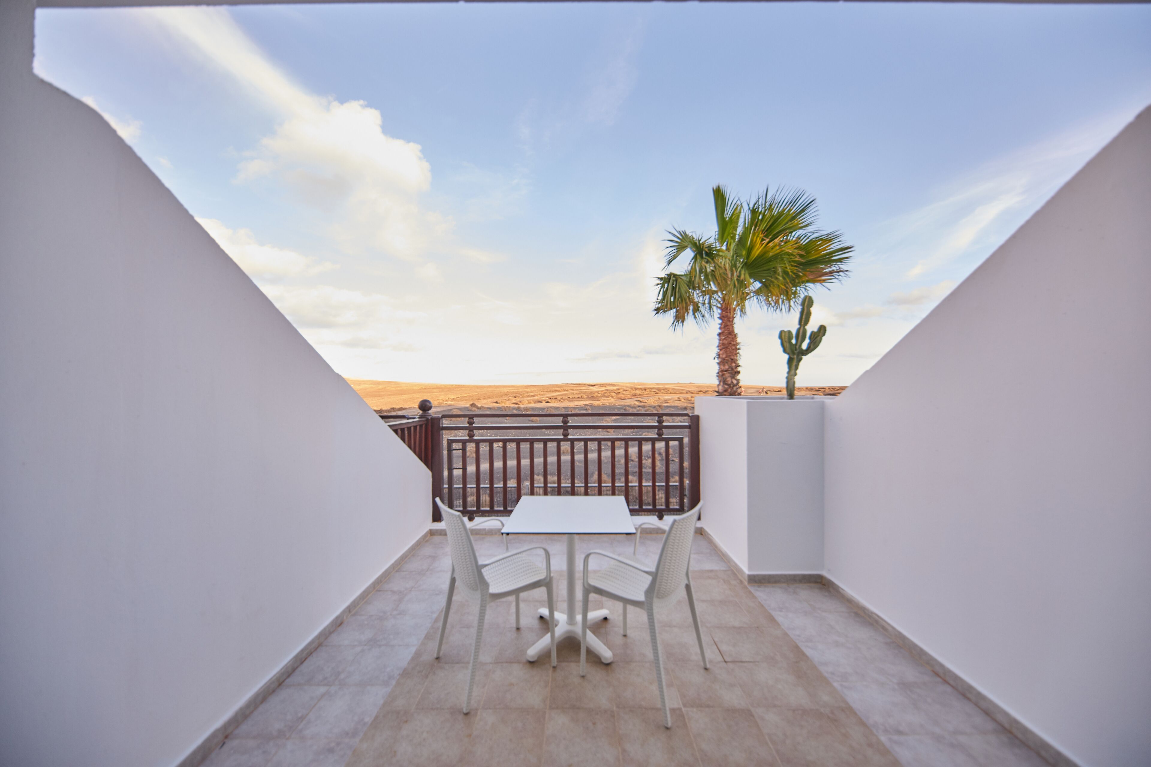 Un balcó amb taula i cadires, una palmera i vista al desert.