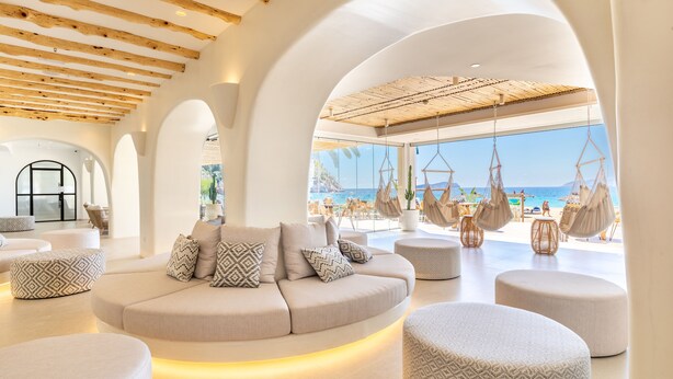 Ein modernes Interieur mit einer gebogenen Couch, Poufs und Hängematten.