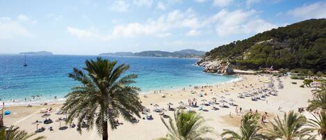 A beach with palm trees, umbrellas, and a clear blue sky.