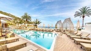 Un espace aménagé au bord de la piscine, avec des chaises longues, des parasols et une vue dégagée sur la mer.
