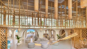 Eine geräumige Lobby im modernen Stil, mit einer zentralen Sitzecke, Sofas und Poufs, einer Holzbodenverkleidung und großen Fenstern mit Blick ins Freie.