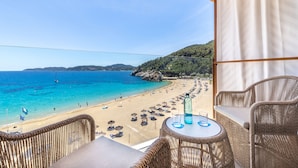 Ein Balkon mit Korbmöbeln mit Blick auf einen Strand mit Sonnenschirmen und Menschen.