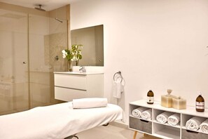 Een moderne badkamer met een douchecabine van glas, een grote spiegel, een wastafelmeubel en netjes opgeborgen handdoeken en toiletartikelen op planken.