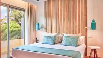 Un dormitorio con una cama grande, cabecera de madera, una mesita redonda y vista a palmeras a través de una puerta corrediza de vidrio.