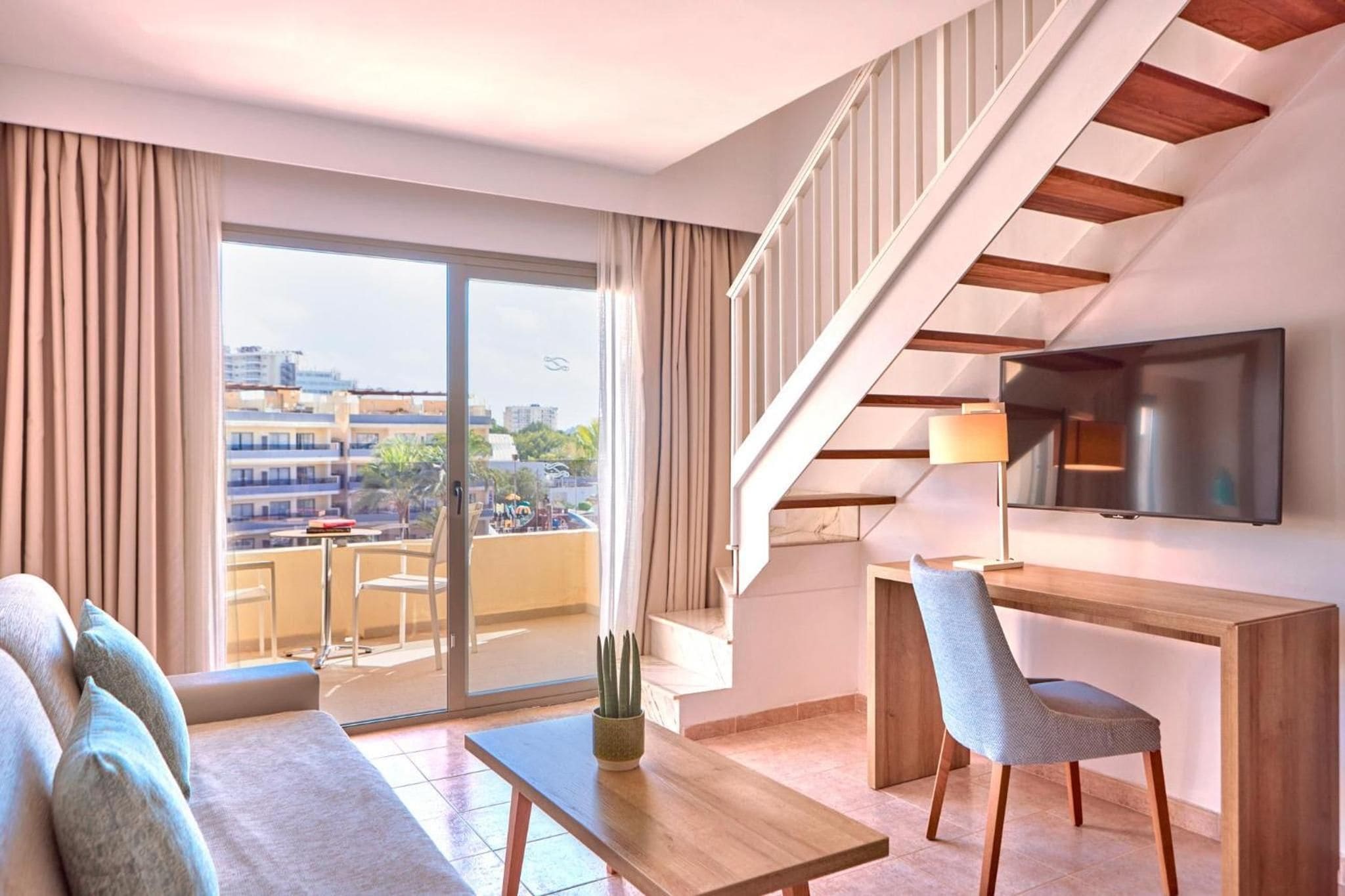 A modern hotel room with a balcony, a desk, a chair, and a TV.