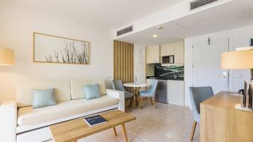 A modern living room with a sofa, coffee table, and chairs. There is a kitchen area with a microwave and cabinets.