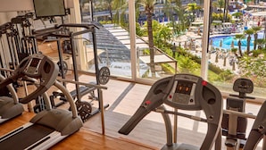 A gym with treadmills, weight machines, and a large window overlooking a pool and outdoor area. - Zafiro Palmanova (Calvia)
