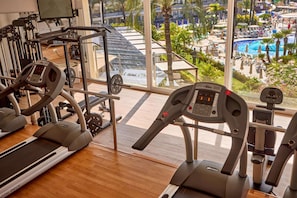 A gym with treadmills, weight machines, and a large window overlooking a pool and outdoor area. - Zafiro Palmanova (Calvia)