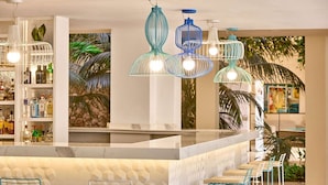 Zona de bar con encimera de mármol blanco, lámparas colgantes azules y blancas, y barra surtida con diversas botellas.
