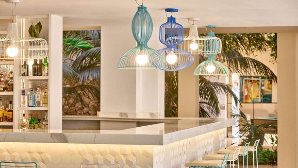 A bar area with a white marble countertop, blue and white hanging pendant lights, and a bar stocked with various bottles. - Zafiro Palmanova (Calvia)