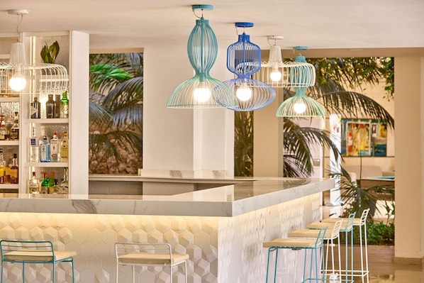 A bar area with a white marble countertop, blue and white hanging pendant lights, and a bar stocked with various bottles. - Zafiro Palmanova (Calvia)