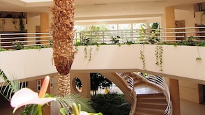 Un atrio de varios niveles con una escalera central, rodeado de vegetación exuberante y una palmera alta.