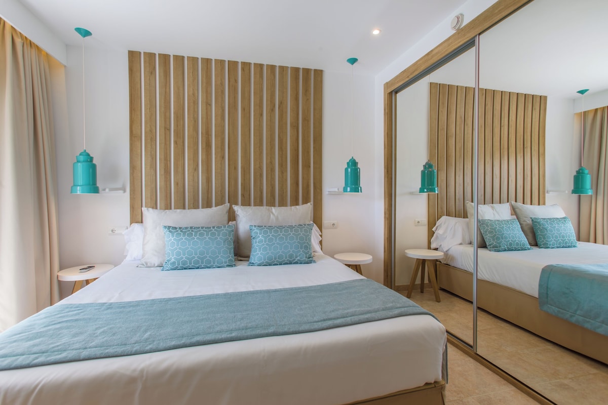 Une chambre d’hôtel avec un grand lit, une petite table ronde, un miroir et deux lampes suspendues.