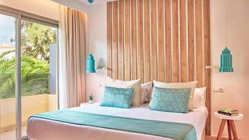 A bedroom with a large bed, a wooden headboard, a view of greenery outside, and a small side table with books.