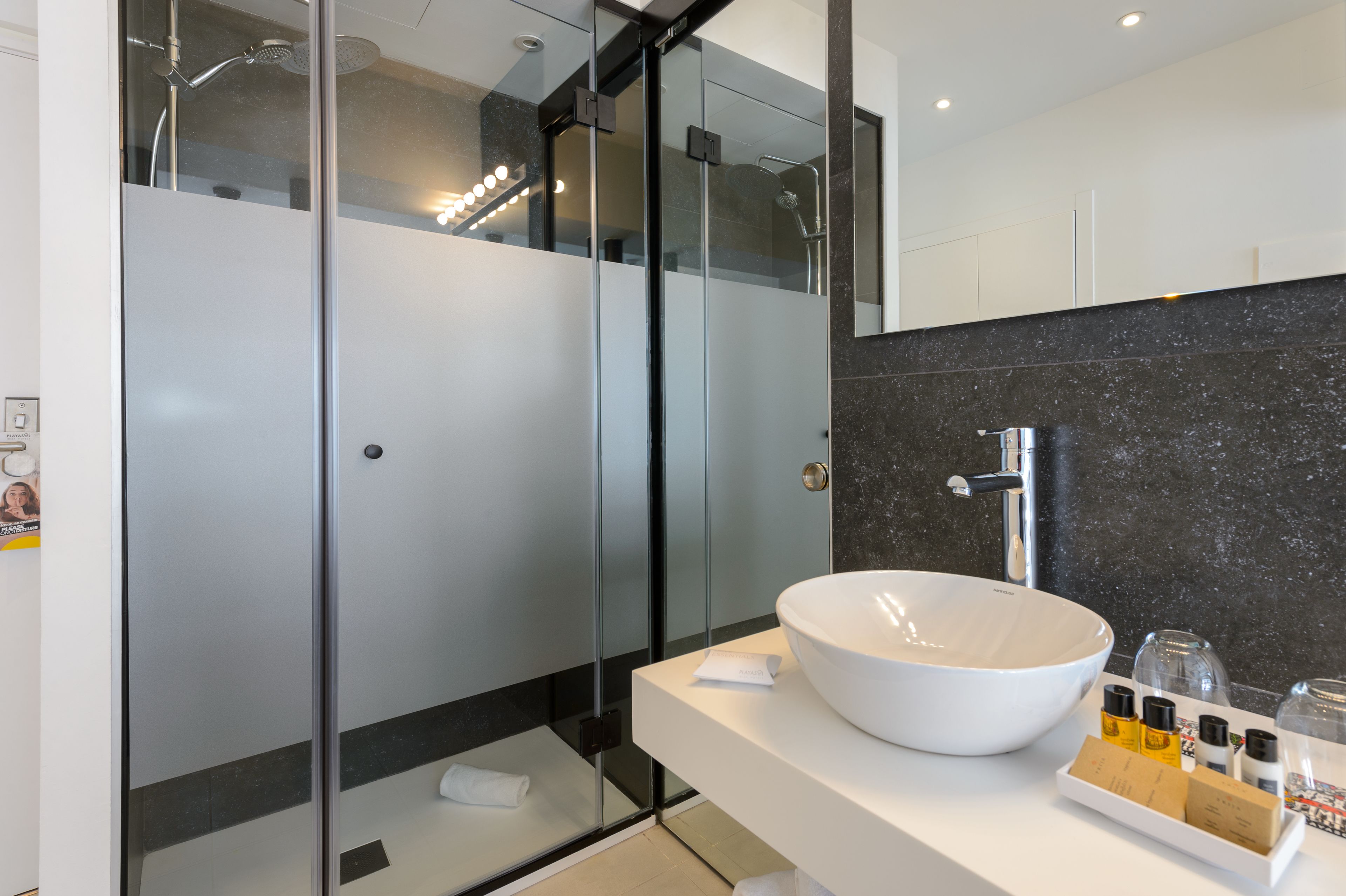 Een moderne badkamer met een douche met glazen wand, een wit wastafelbakje en een zwarte marmeren spatwand.