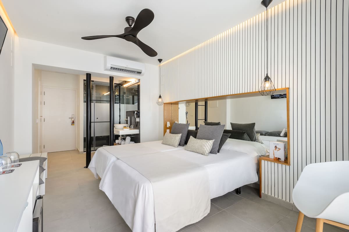 Habitación de hotel moderna con una cama grande, un escritorio, un espejo y un ventilador de techo.