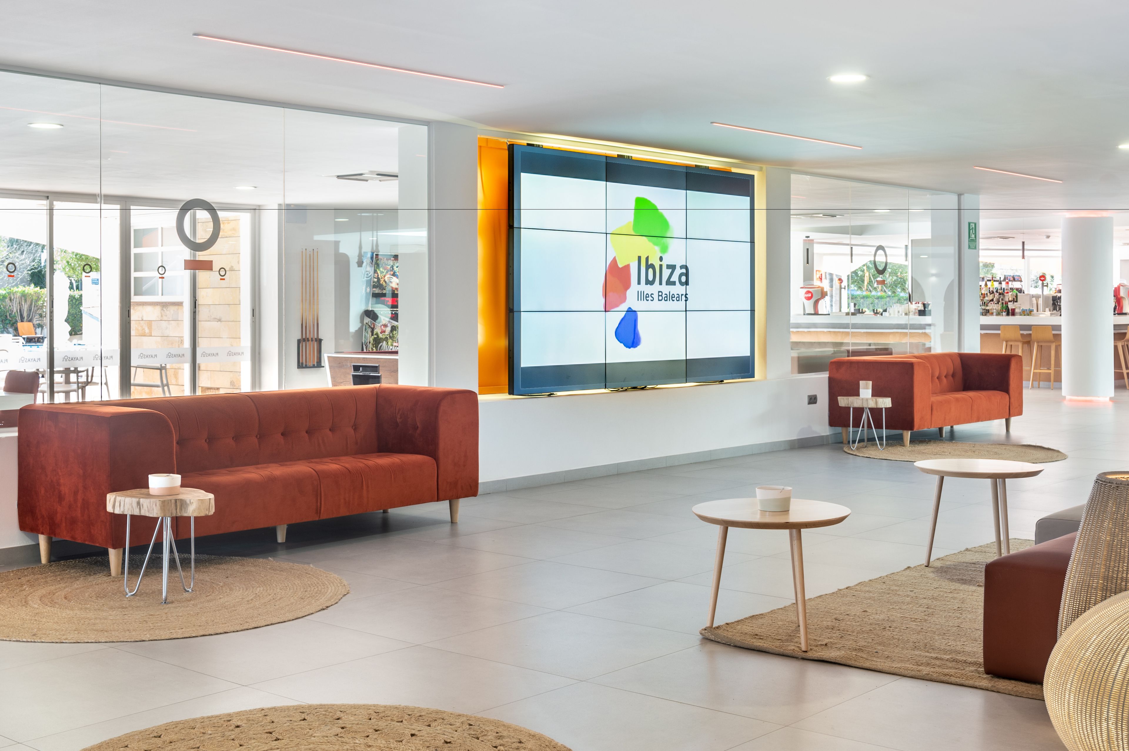 A modern lobby with a large screen displaying the Ibiza logo, comfortable seating areas, and a clean, bright interior.